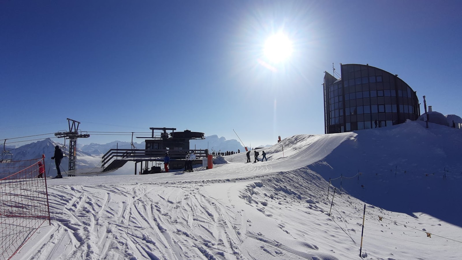 Skiers on a wide sunny piste above Leysin with the Dents du Midi across the valley