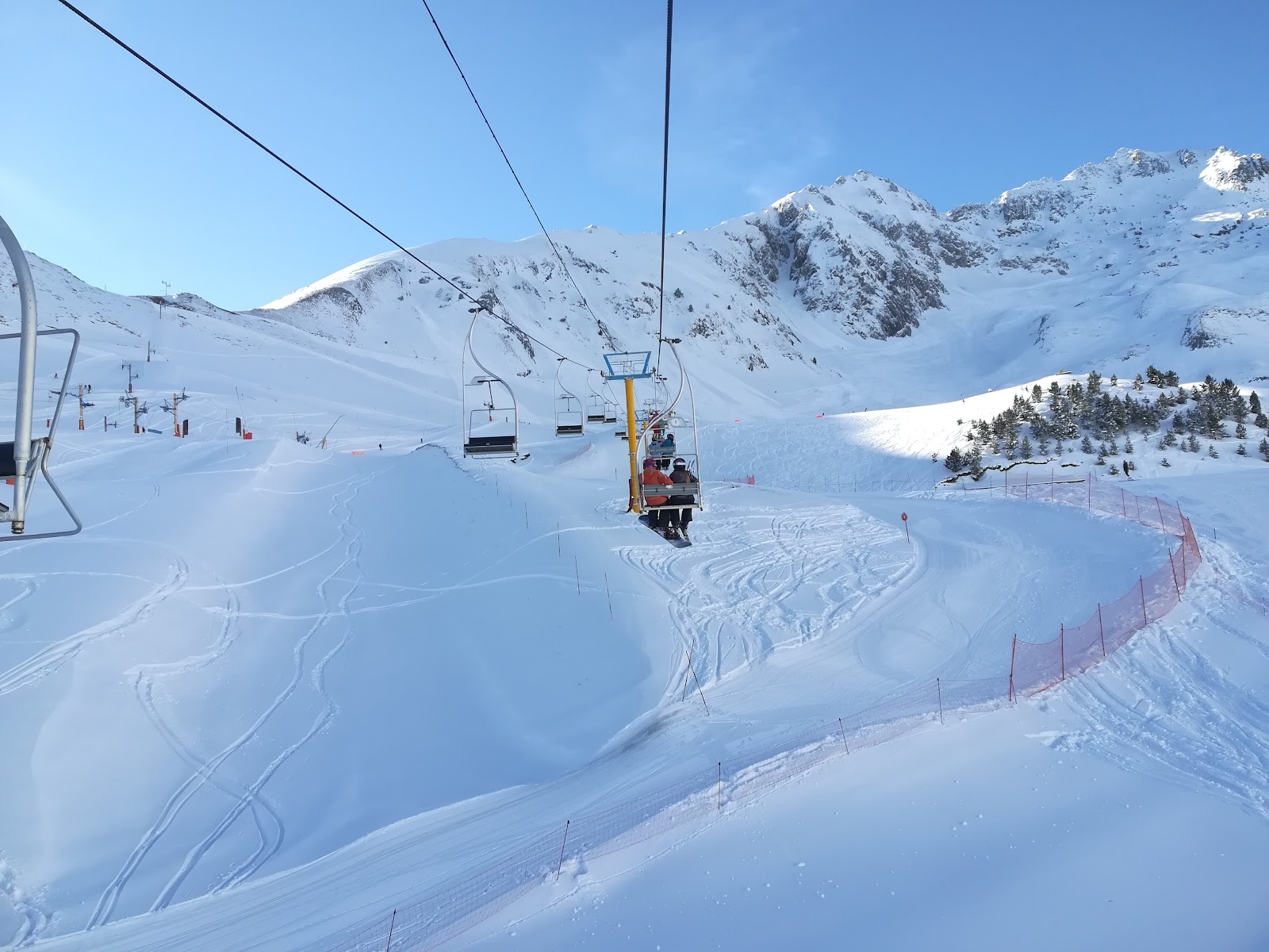 Skiers on a wide sunny blue piste in the Luz Ardiden bowl