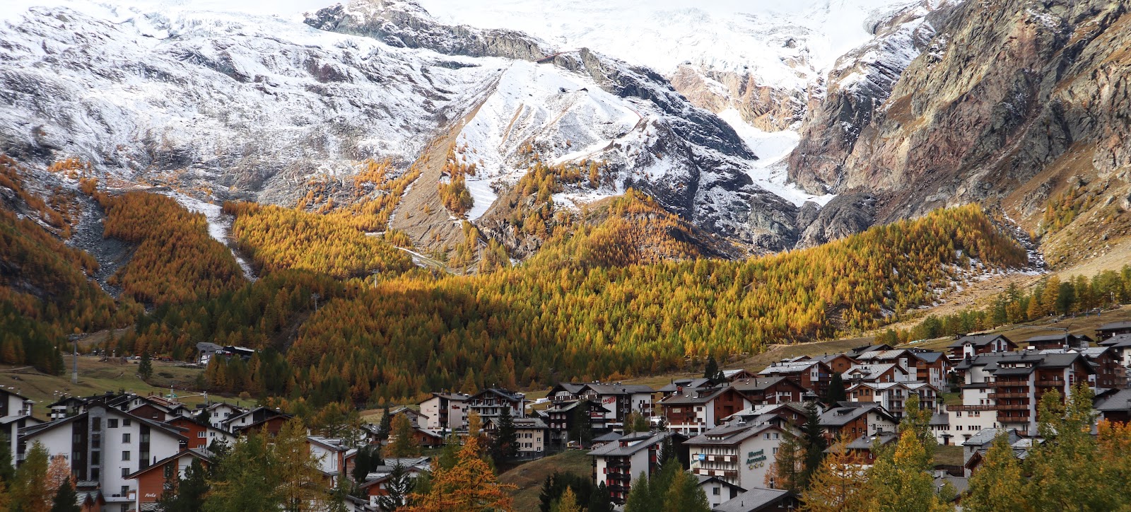 Skiers cruising a wide sunny glacier piste high above a Valais village