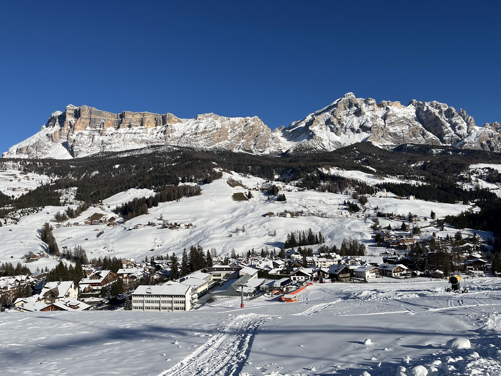 Skiers cruising wide sunny runs with dramatic Dolomite scenery at San Cassiano