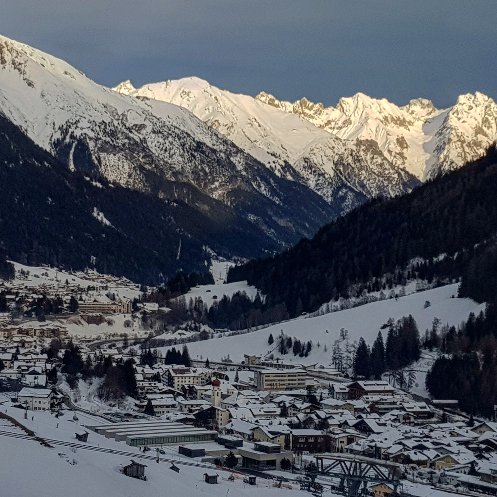 Steep red pistes dropping toward the village of St Anton am Arlberg under snow