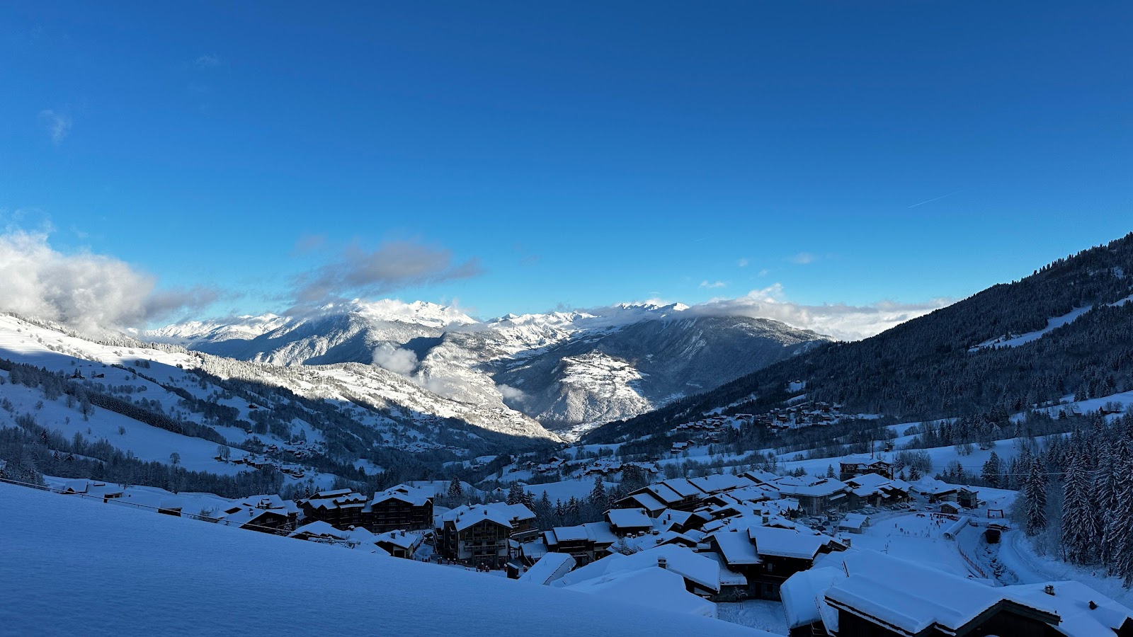 Skiers on wide gentle sunny pistes above the treeline at Valmorel