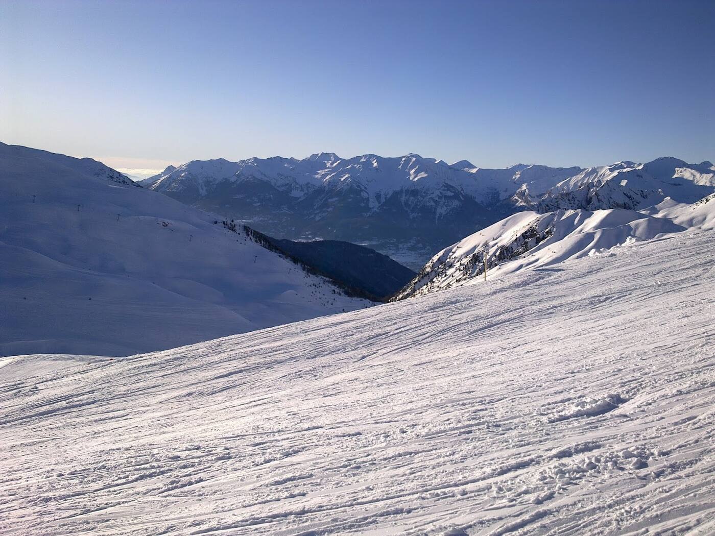Skiers descending a wide groomed piste between larch trees at Vars